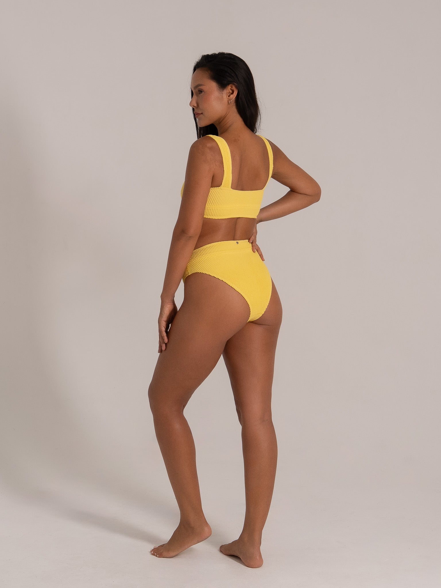 Side view of model in mustard yellow textured swimwear set featuring scoop neckline and supportive thick straps