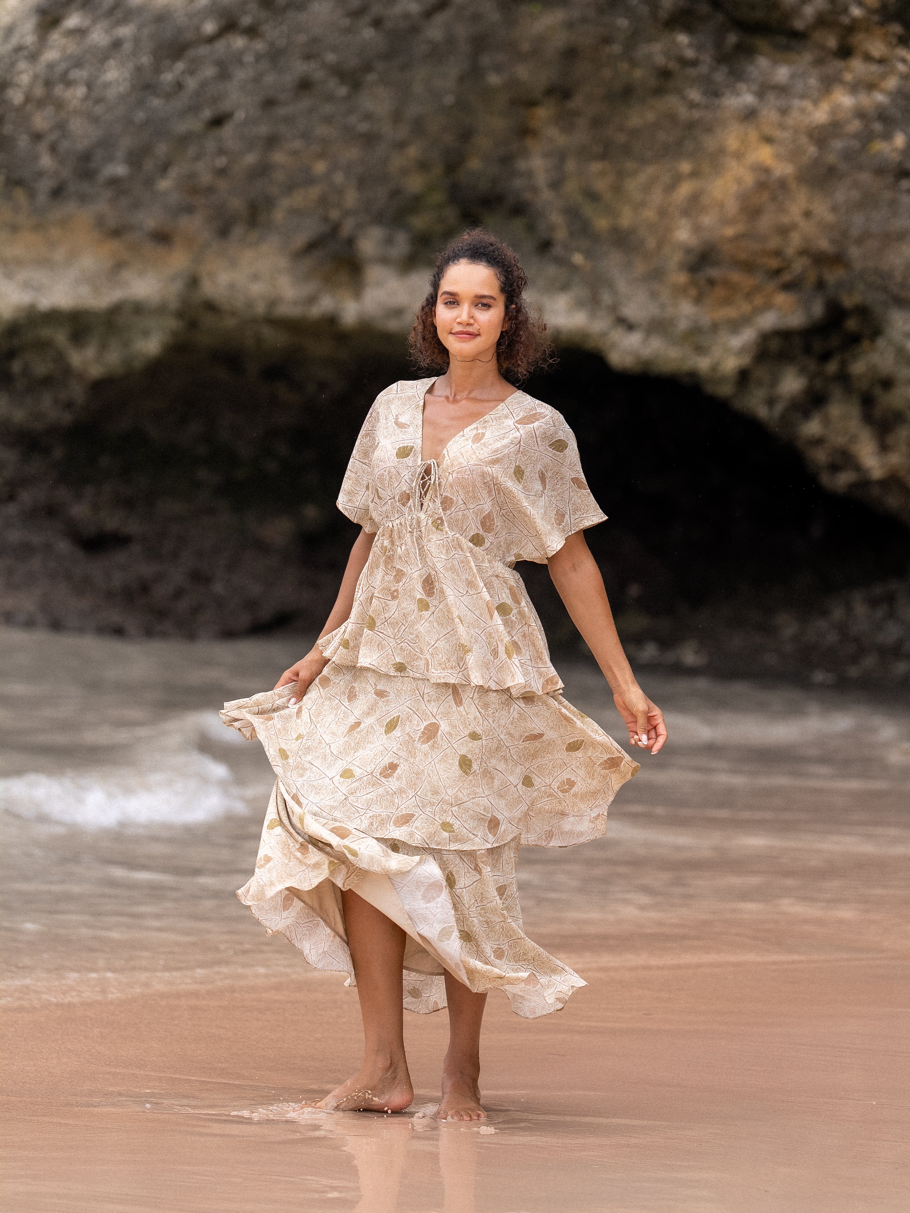 Woman walking on the beach wearing OCEAN MYSTERY muted yellow tiered maxi dress with vintage leaf print.