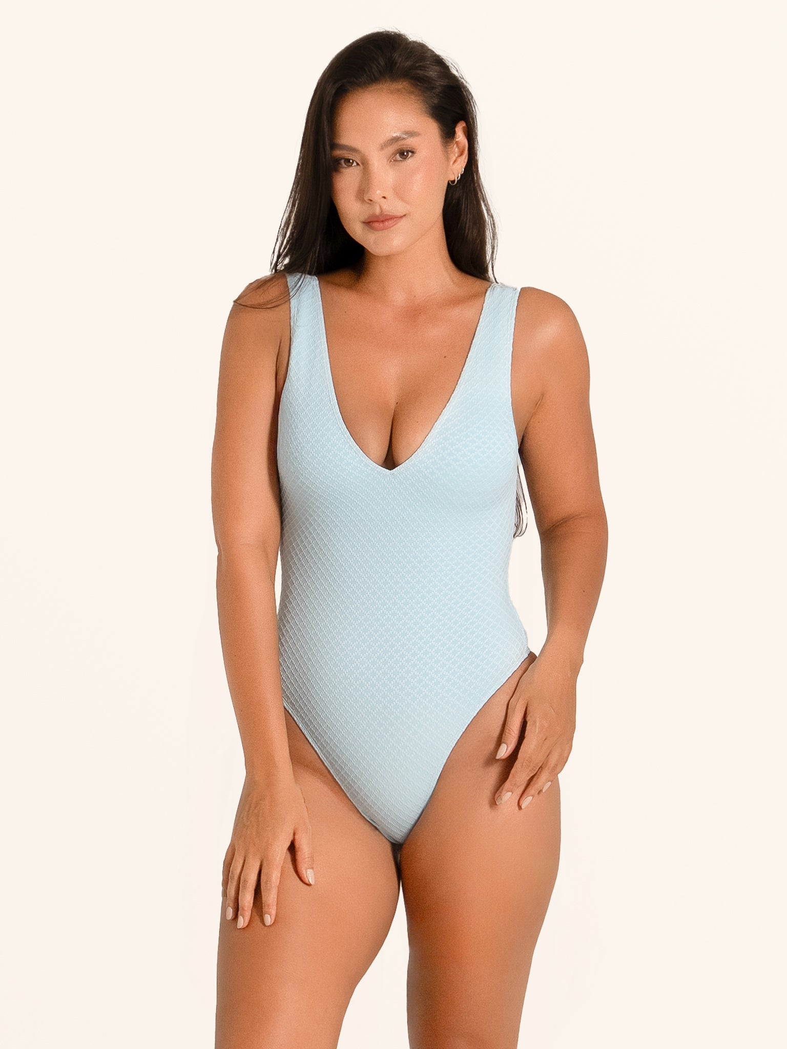 Front view of woman wearing baby blue textured one piece swimsuit with deep V neckline.