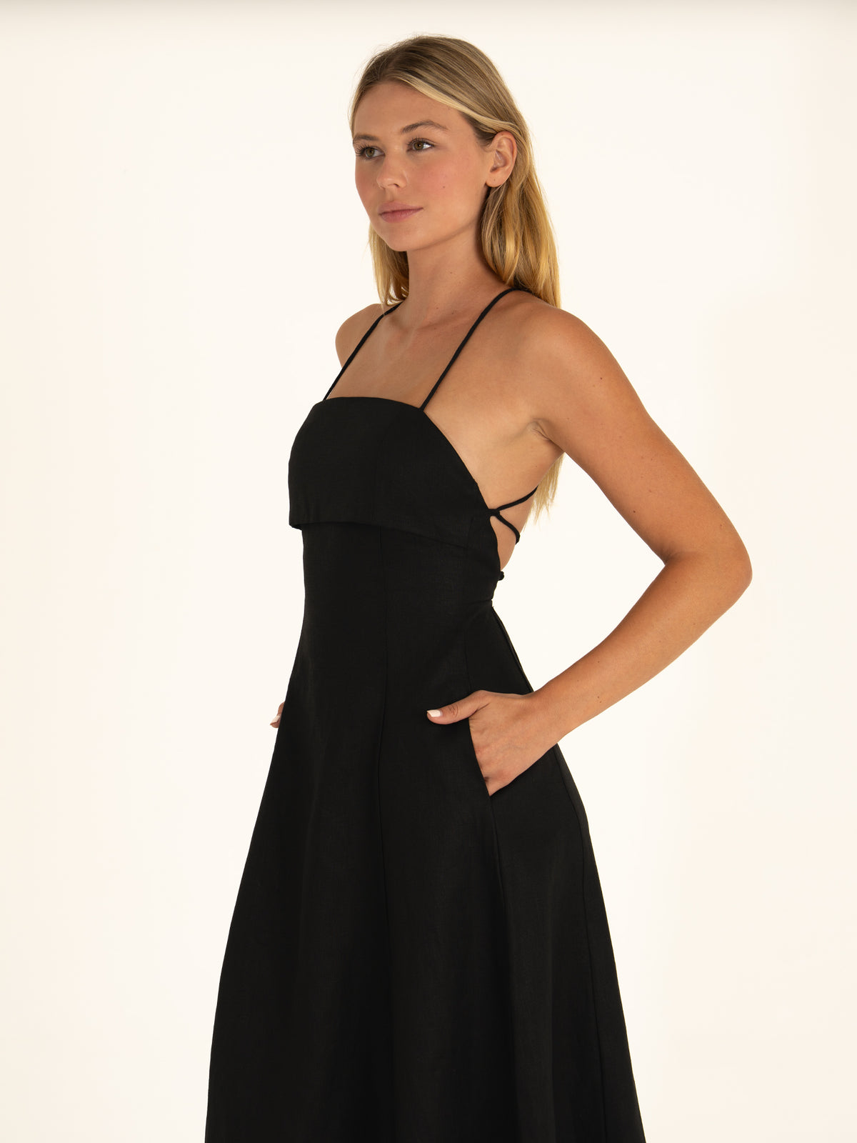 Woman posing with her hands inside the hidden side pockets of the Onyx linen dress, demonstrating its blend of quiet luxury and practicality.
