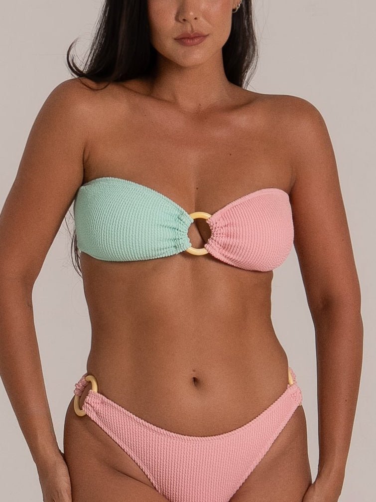 Close-up of a pastel pink and mint green bandeau bikini with central ring and matching high leg bottom with side rings