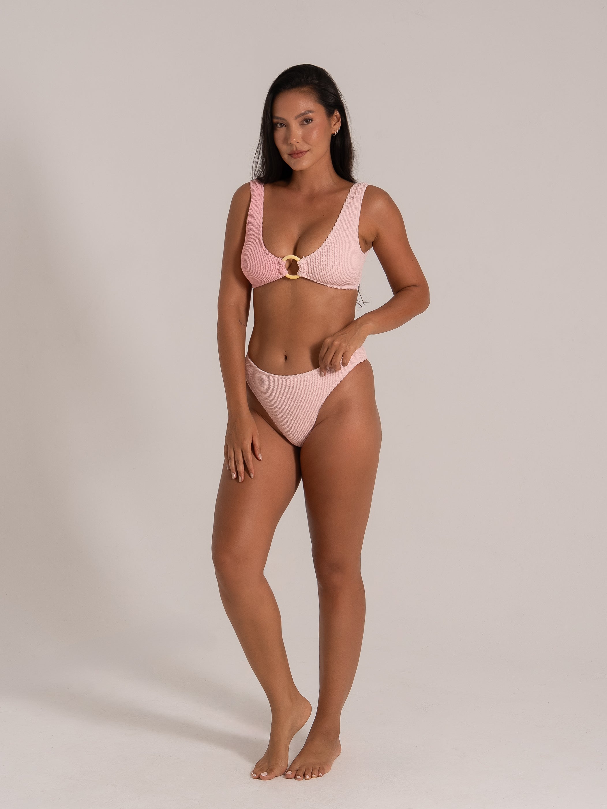 Model in a pink textured bikini set featuring a central ring detail, standing in a relaxed pose.