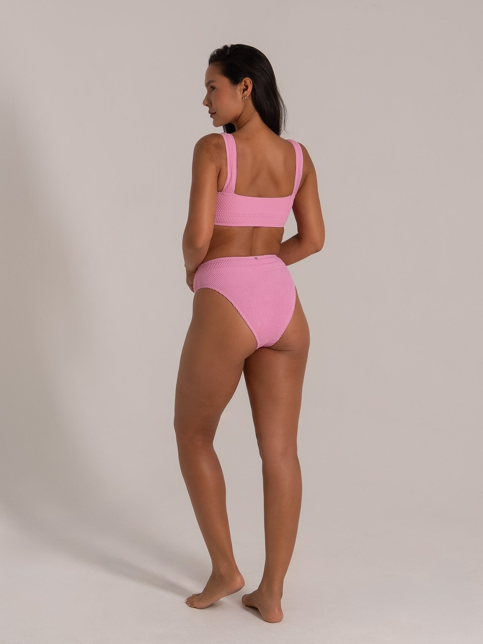 Side view of model showcasing pink textured bikini set with wide straps and high waist bottom