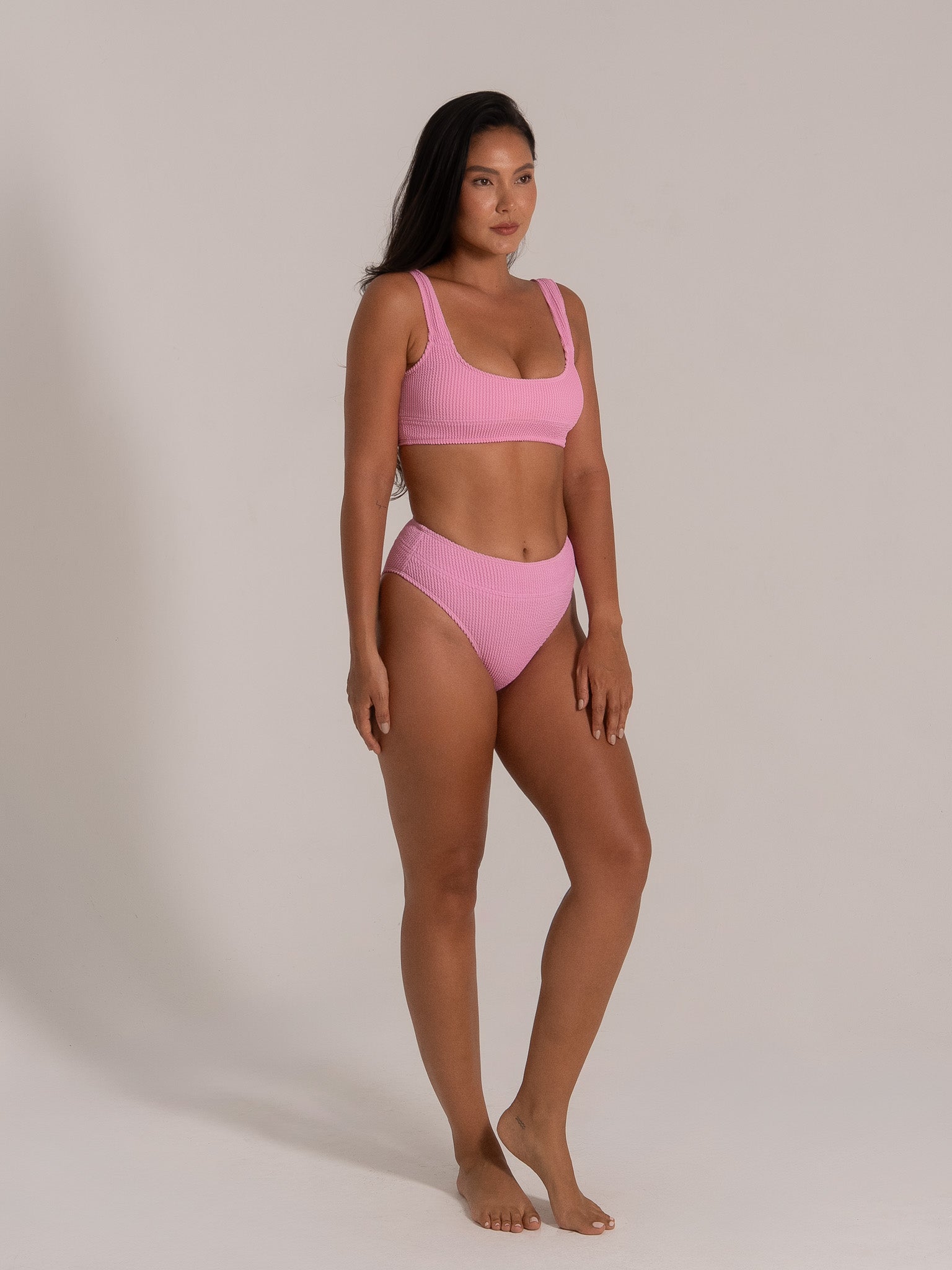Model standing in pink square neck bikini top and high waist bottom made from textured fabric