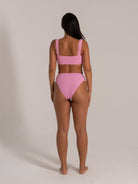 Back view of woman wearing pink textured square neck bikini top and high waisted bikini bottom