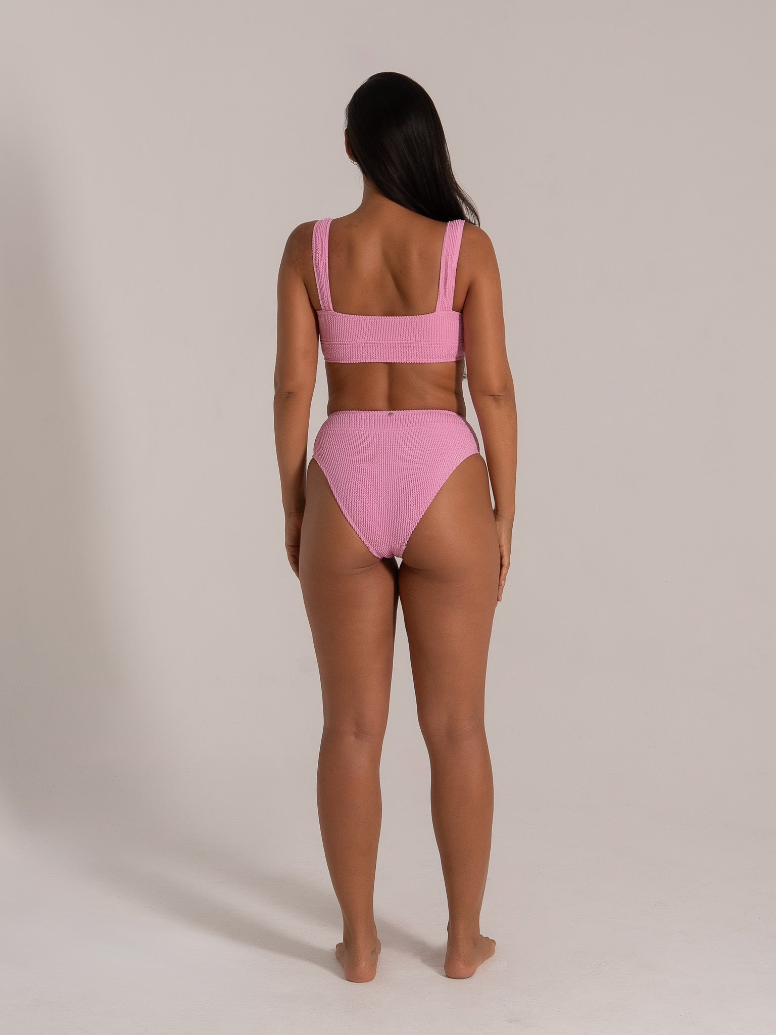 Back view of woman wearing pink textured square neck bikini top and high waisted bikini bottom