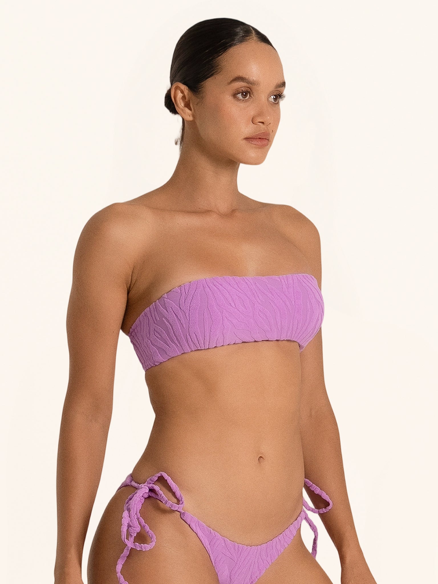Side pose of purple bandeau bikini top showing strapless ruched detail.