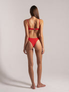 Back view of a woman modeling a red bikini with high-leg bottoms and adjustable shoulder straps, photographed in a studio setting.