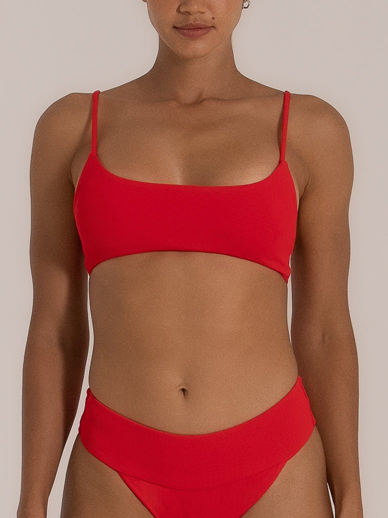 Front view of a woman wearing a bold red bikini set featuring a square neckline top with thin adjustable straps and a high-waisted textured bottom for a flattering, modern beach look.