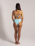 Back view of a woman wearing a shimmering aqua high-waisted bikini with textured wave-like patterns and tie-back straps