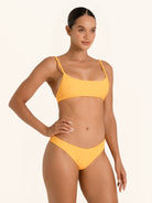 Woman posing in mustard yellow square neck bikini top with ruched detail and crop fit.