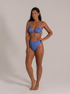 Model posing confidently in a high-waisted blue bikini with subtle texture and ring detail.