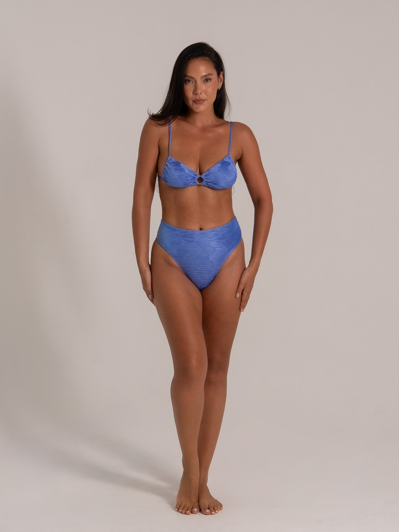 Front view of a model wearing a textured blue bikini set with high-waist bottoms and underwire top.