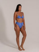 Side front pose of a woman in a textured blue high-waisted bikini with supportive top.
