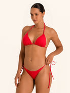 Model posing in red triangle bikini top with adjustable halter neck ties.