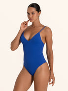 Side pose of woman in blue textured V neck one piece swimsuit with flattering fit.