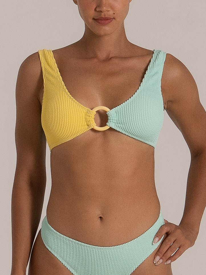 Close-up of a yellow and mint green colorblock bikini top with a central ring detail, paired with a matching mint green textured bottom.