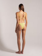 Model showing back view of yellow textured triangle bikini with halter neck and tie-back straps.