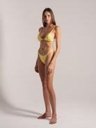 Yellow textured bikini set with halter top and side-tie bottoms, model posing at an angle.