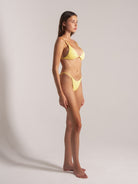Side view of model wearing yellow halter triangle bikini top and tie-side bottoms with textured fabric.