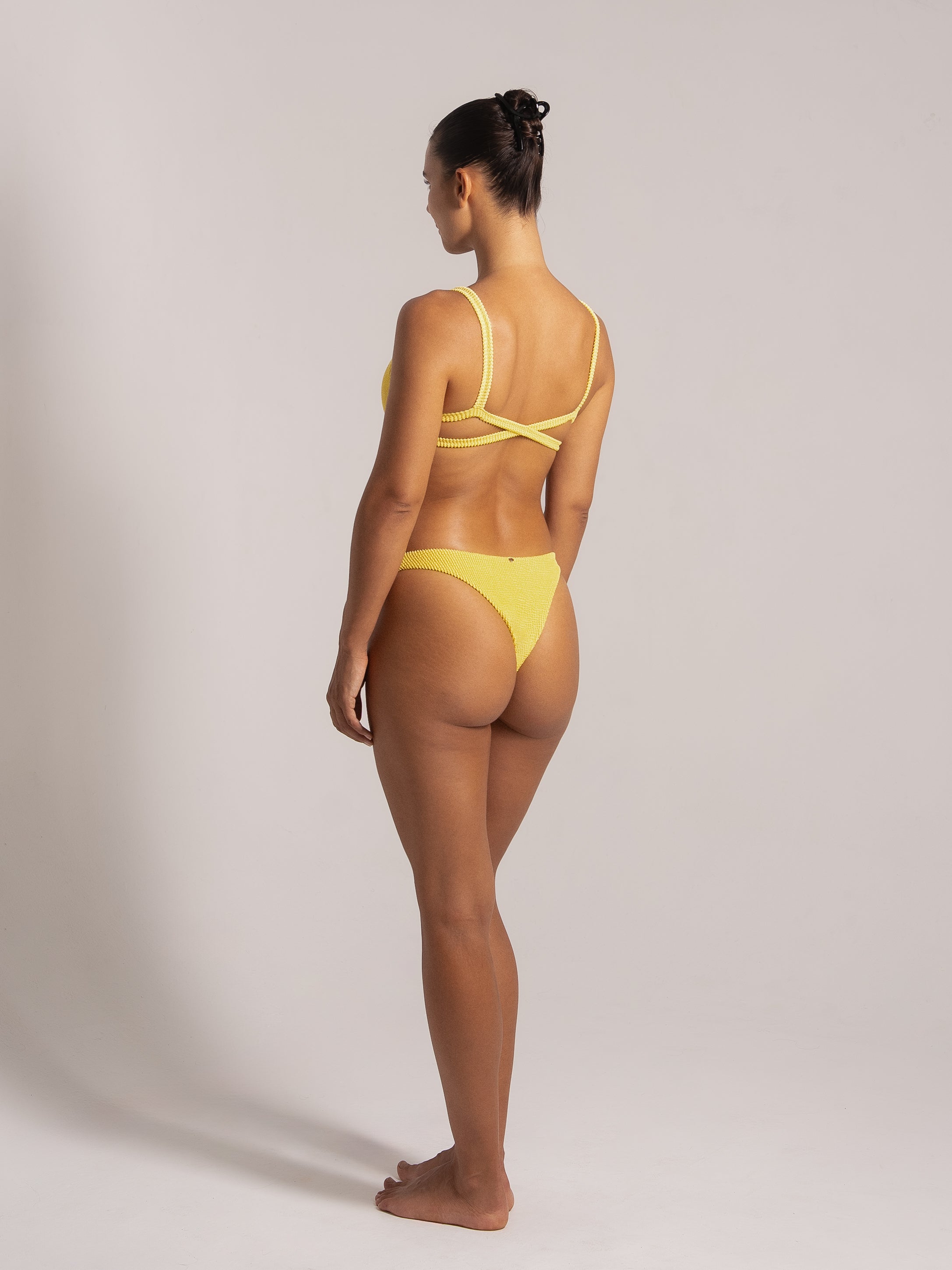 Angled rear view of yellow textured bikini featuring a crisscross back and cheeky bottom fit.