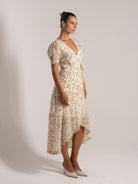 Ocean Mystery white floral V-neck dress with puff sleeves and asymmetrical hem featuring orange/green blooms.