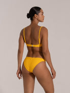 A confident woman showcasing a vibrant yellow bikini with textured fabric, highlighting her toned physique in a studio setting. The image emphasizes sleek hair, minimalistic background, and the garment's stylish design, perfect for fashion or lifestyle content.