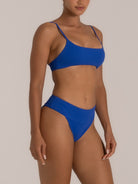 Angled view of minimal scoop bikini top and high cut textured bottom in blue