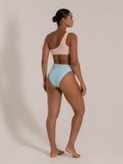 Angled back view of an asymmetric bikini with a pink textured top and sky blue high-leg bottoms.