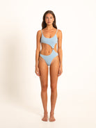 Model in light blue textured one-piece swimsuit with ring cutout design, front-facing pose