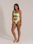 Front view of woman wearing an asymmetric one-piece swimsuit with double waist cutouts in green-yellow print