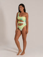 Side view of a woman modeling an asymmetrical one piece swimsuit in green and yellow tie-dye with bold side cut-outs.