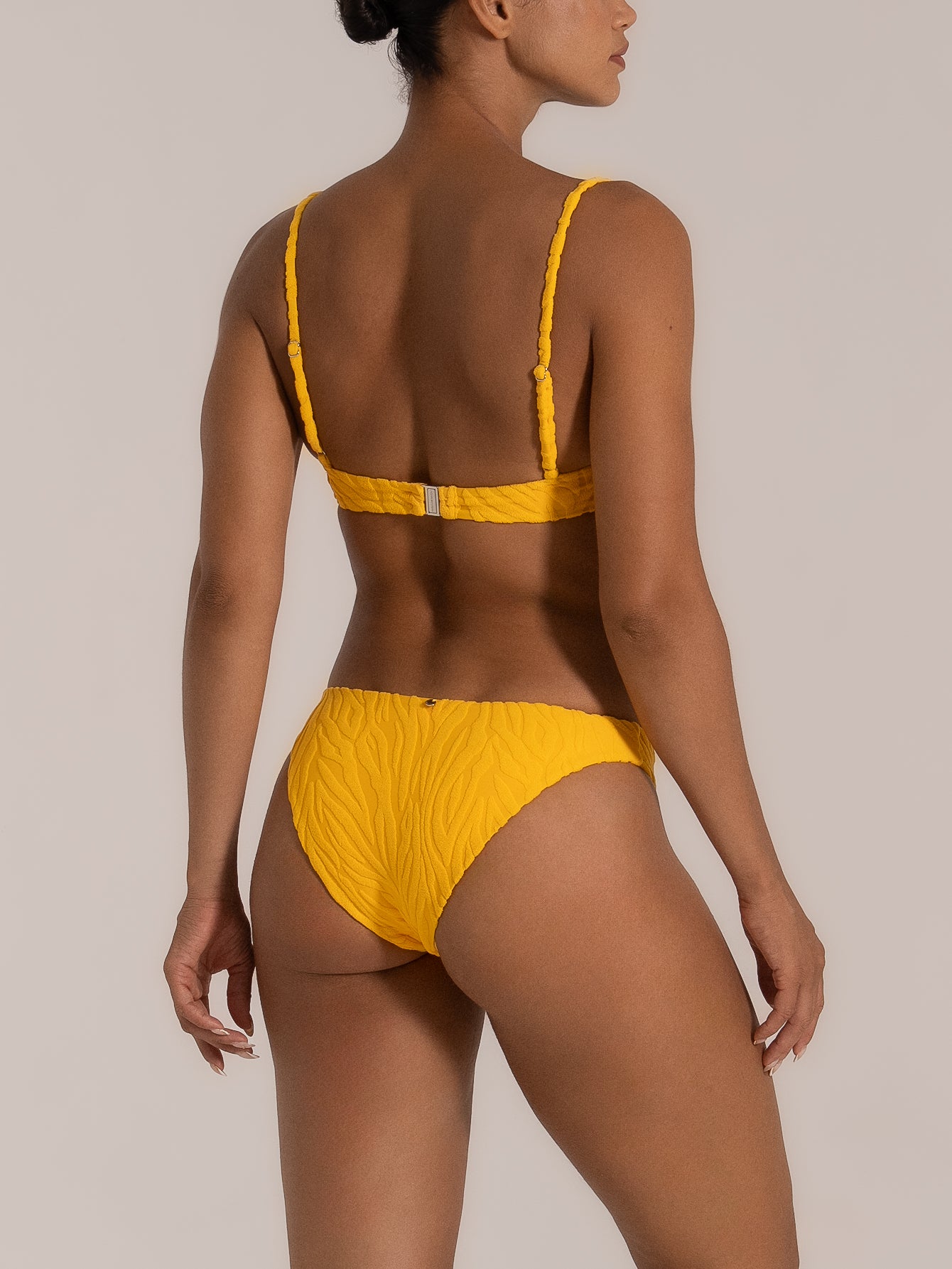 Side-back angle of a yellow bikini bottom featuring textured fabric and cheeky coverage.