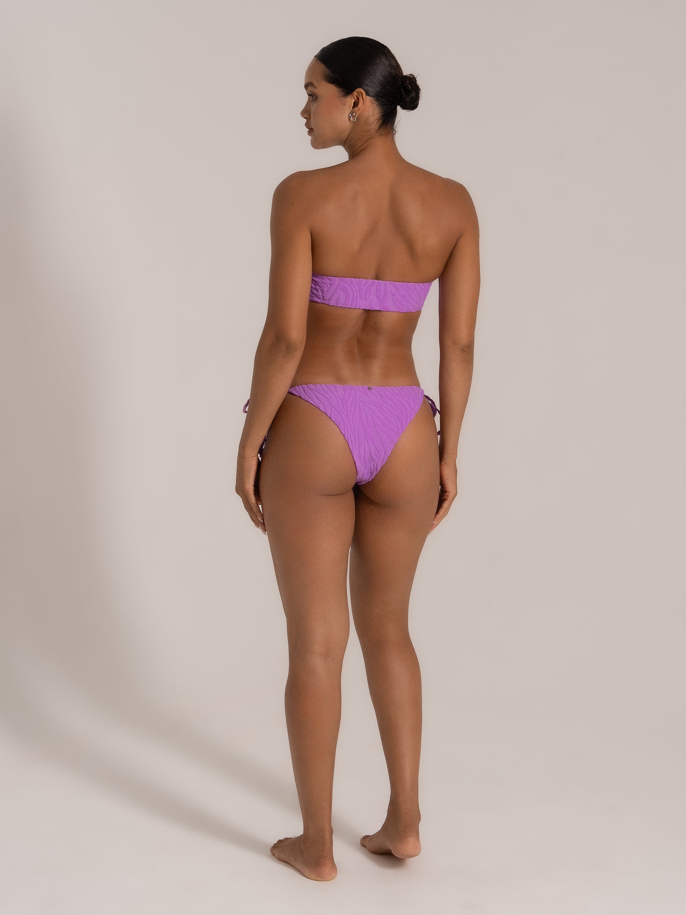 Model wearing purple textured bandeau bikini set, back view