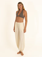 Effortless beach-to-bistro styling featuring a charcoal gray nylon bikini top worn as a crop top with flowy white pants.