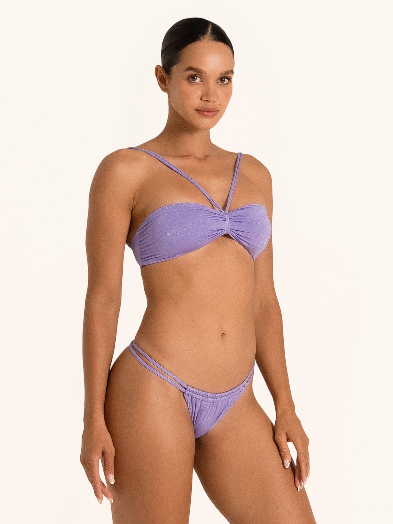 Side front angle of woman wearing purple bikini bottom with minimal coverage fit.