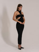 Side angle of a fitted black glitter halter dress with front cutout and high neck detail.
