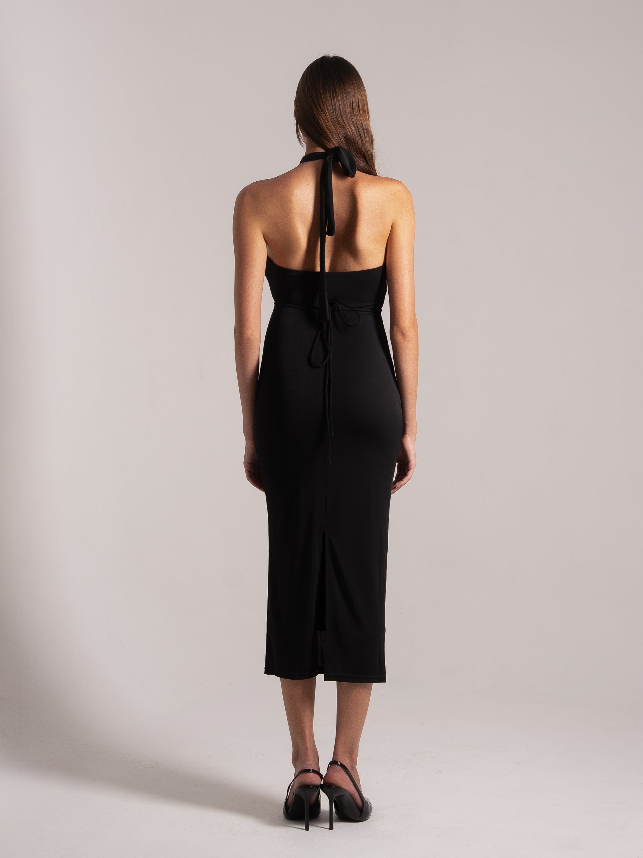 Angled back view of black halter tie‑back cutout midi dress with slit