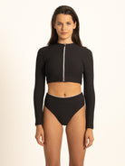 Front view of a woman wearing the Ocean Mystery black long-sleeve rash guard with the front zip fully closed, offering maximum sun protection and a sleek athletic fit.