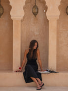 Woman wearing black maxi dress seated outdoors in lifestyle setting