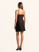 Rear side profile of black mini dress with slim straps and slit hem