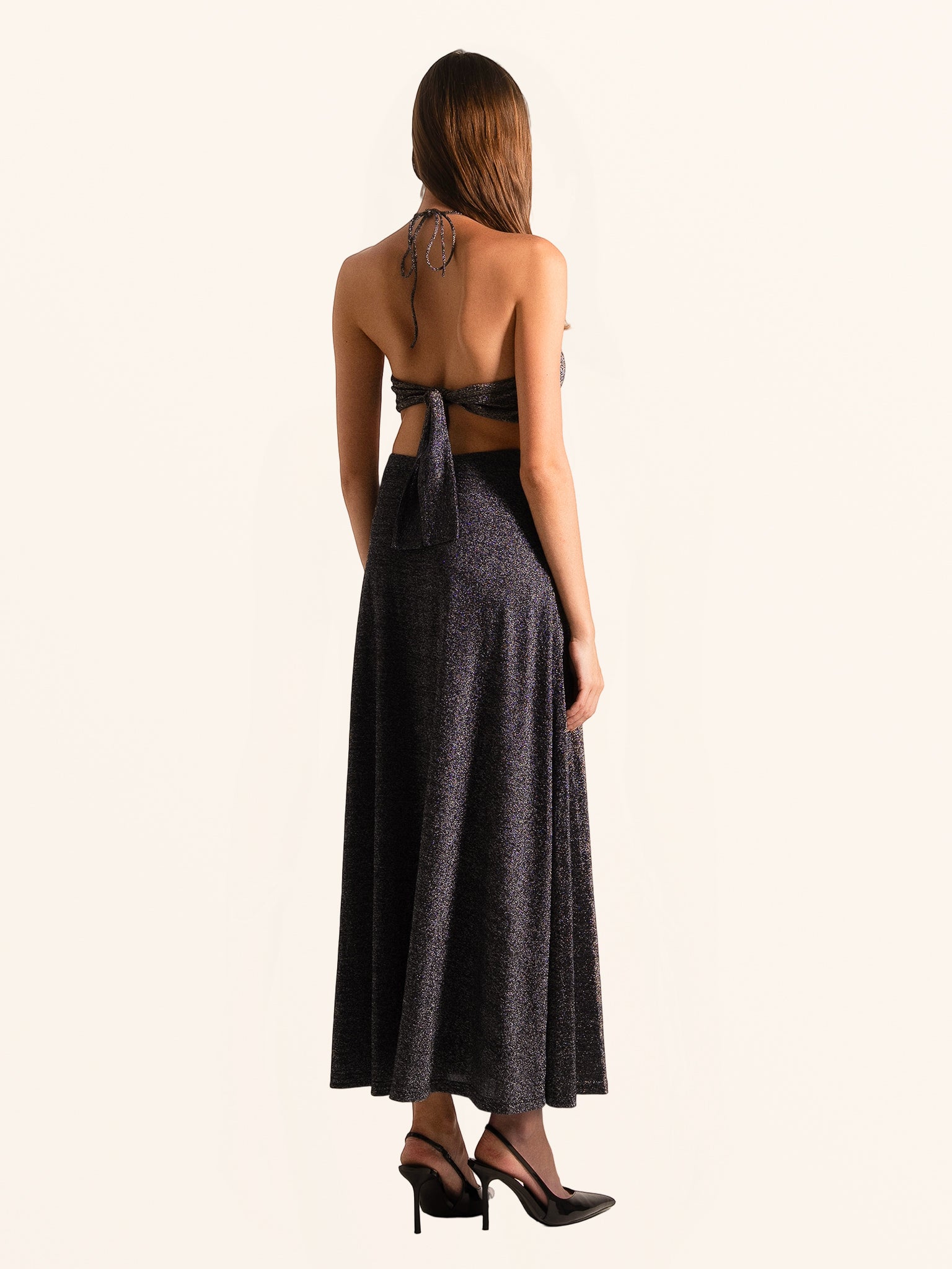 Rear side angle of black sequined halter maxi dress with flowing skirt