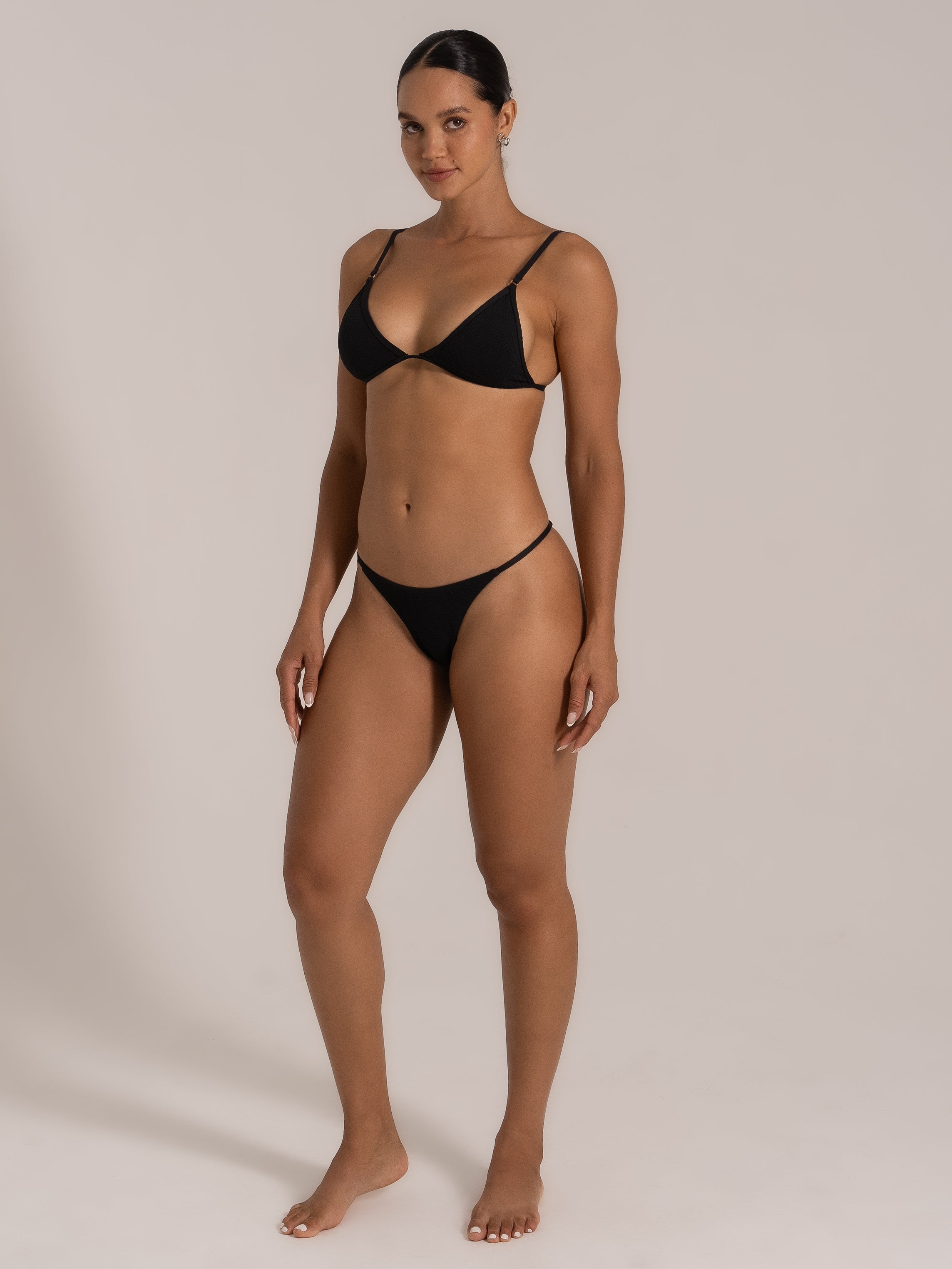 Angled front view of model in black triangle bikini set showing v-neckline and cheeky bottom