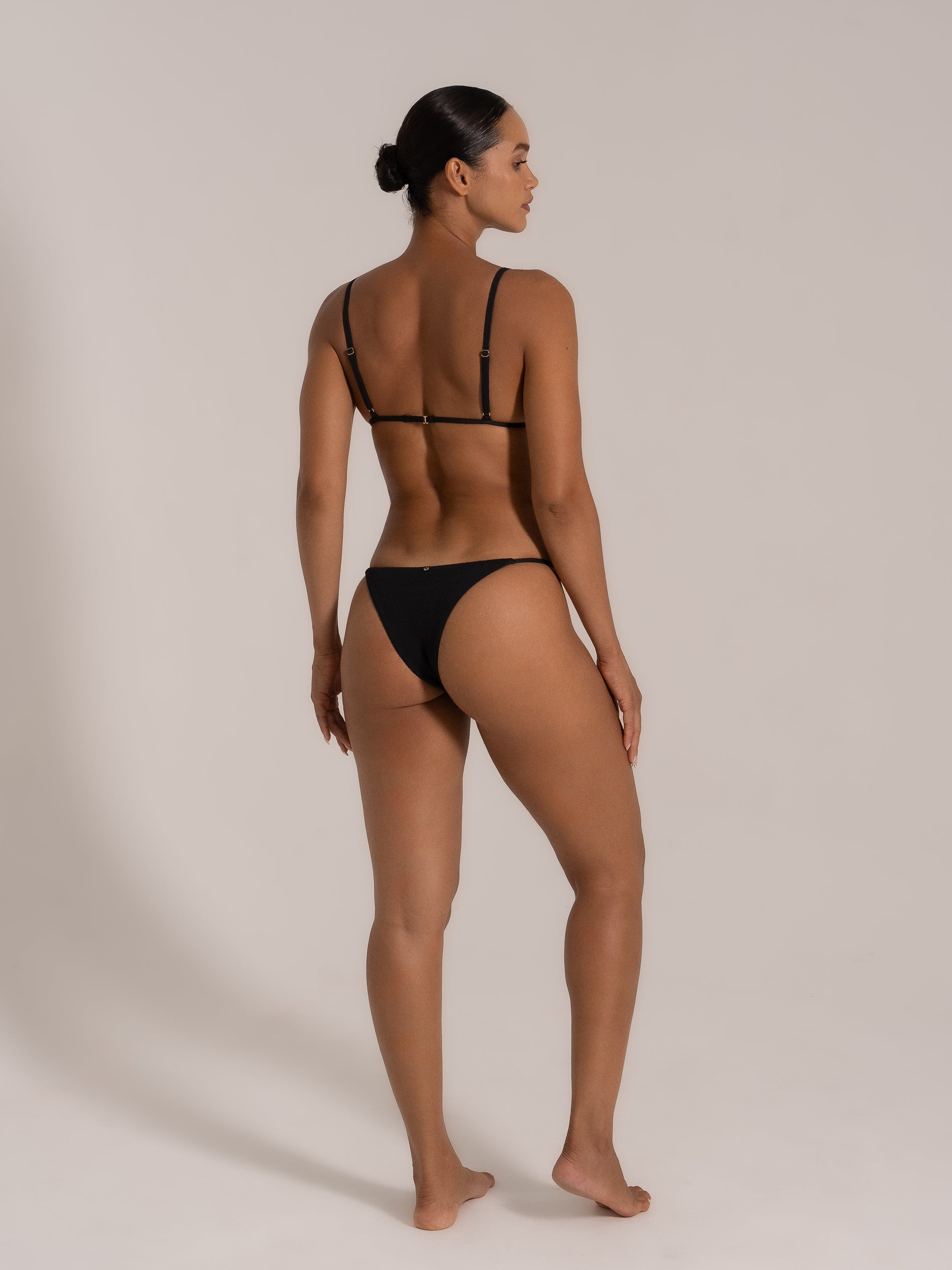 Side back view of model wearing a black triangle bikini set with thin straps and textured fabric