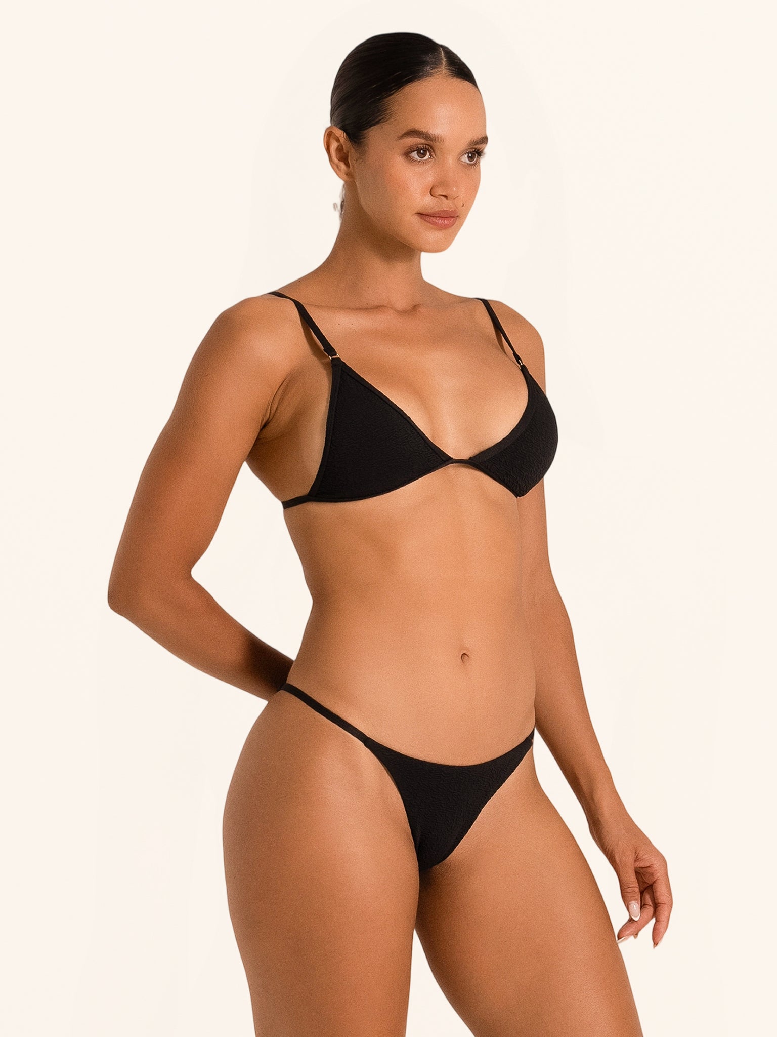 Woman posing in black triangle bikini top with sleek minimal coverage design.