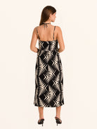 Rear side angle of black and white leaf print midi dress with flowy hemline