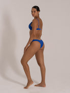 Three-quarter back pose of model in vibrant blue underwire bikini with textured finish