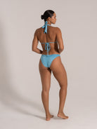 Back view of woman wearing a light blue halter bikini top with adjustable tie straps and ruched cheeky bikini bottom.