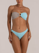 Model in a high-leg textured blue bikini bottom with wooden ring side accents, matching with a unique bandeau top