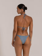 Back view of woman wearing a blue shimmer textured triangle bikini with halter neck and tie-back design